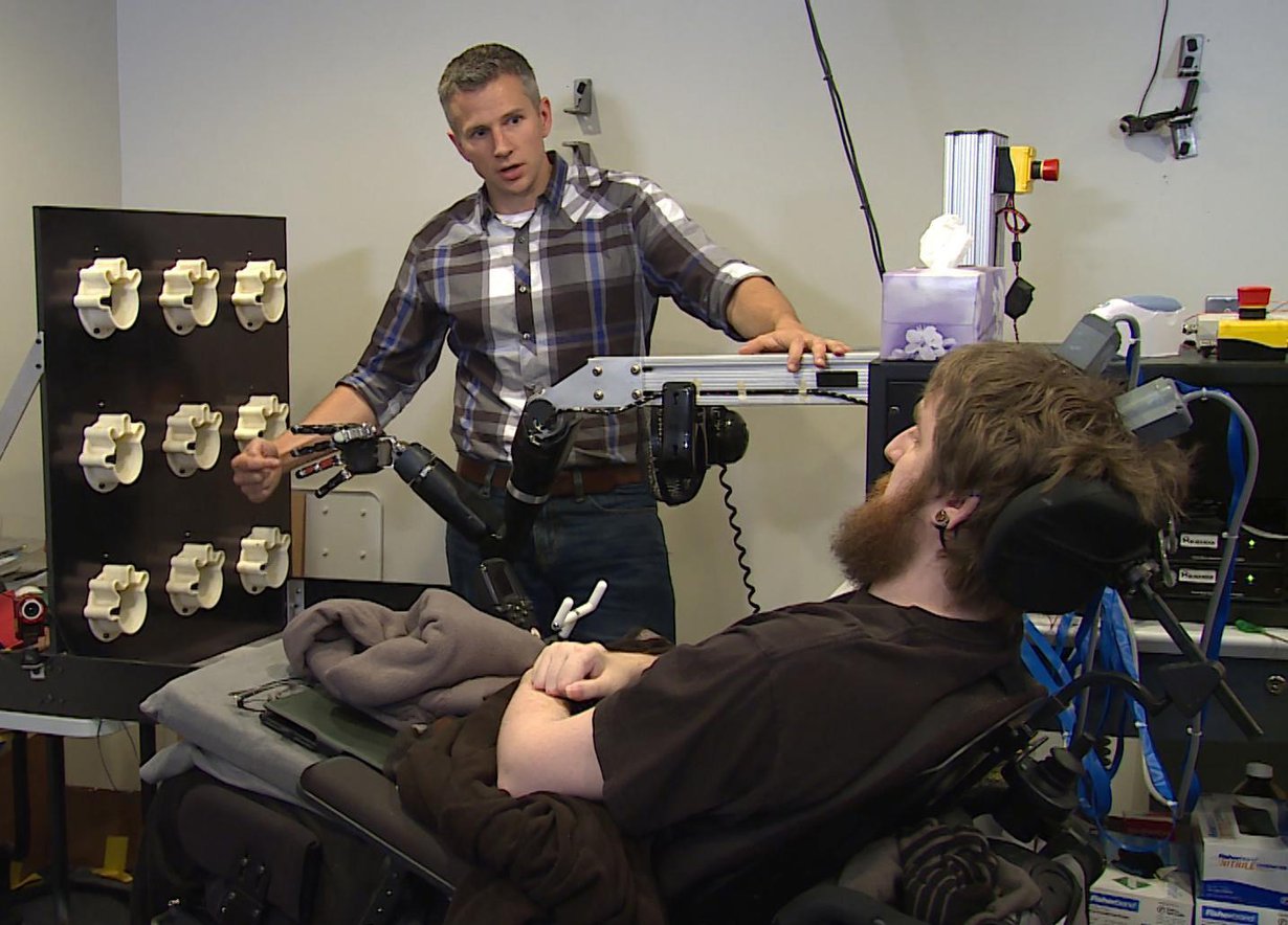 Neliraajahalvaantunut Nathan Copeland (edessä) saa tuntoaistimuksia robottikädestä. Koetta tekee tutkija Rob Gaunt. Kuva: UPMC/Pitt Health Sciences