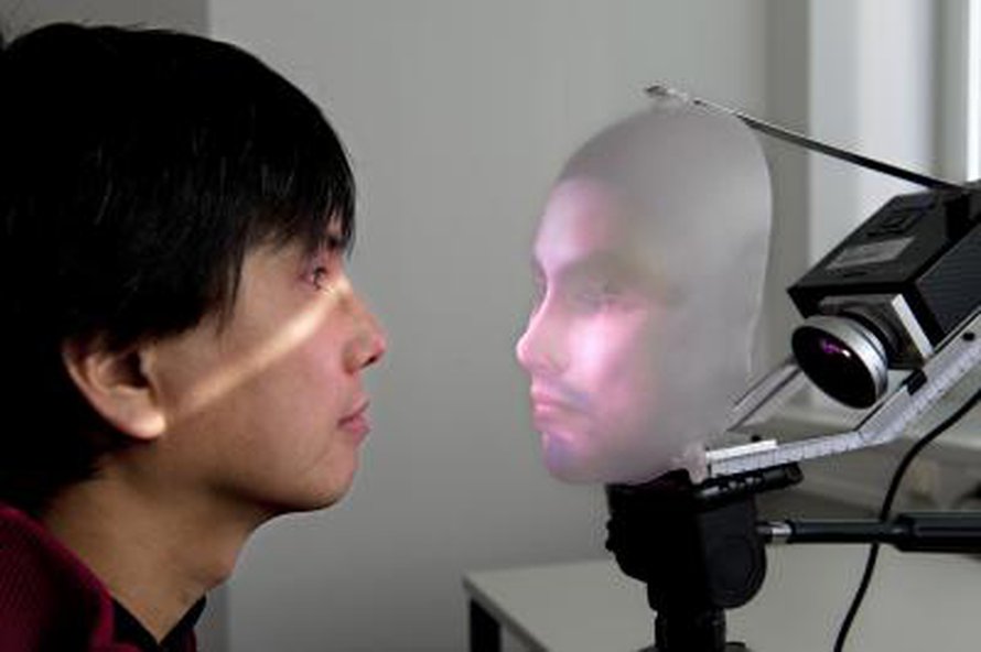 Tutkija Takaaki Kuratate ja robottinaama Mask-bot kasvokkain.