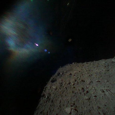 Robotti on lähtenyt kohti asteroidia, jonka pinta näkyy oikealla. Värikäs sumu johtuu auringon heijastuksista. Kuva: <span class="photographer">Japan Aerospace Exploration Agency</span>