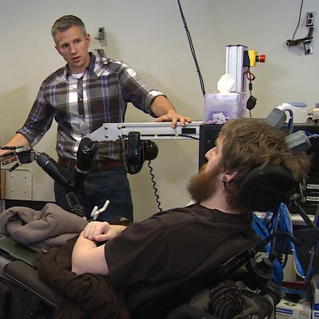Neliraajahalvaantunut Nathan Copeland (edessä) saa tuntoaistimuksia robottikädestä. Koetta tekee tutkija Rob Gaunt. Kuva: <span class="photographer">UPMC/Pitt Health Sciences</span>